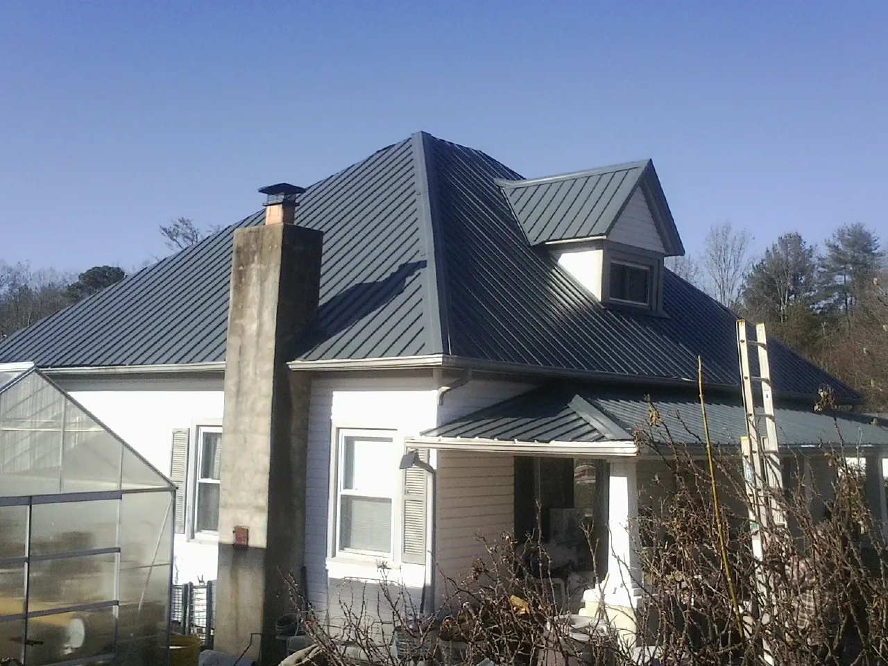 Dark blue standing seam metal roof on a white farmhouse with dormer — Slate & Tile Roof Repair by Roofing Brothers in Weldon