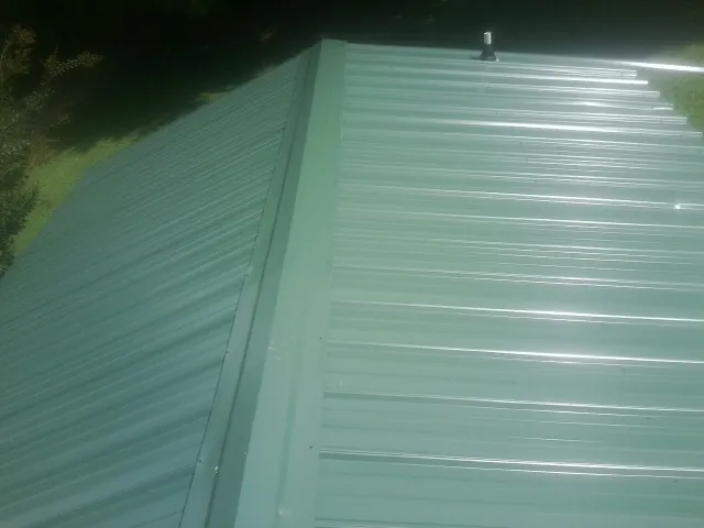 New green metal panels meeting at the ridge of a roof — Flat Roof Repair work by our crew in Weldon